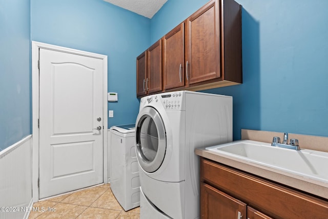 washroom featuring a textured ceiling, washer and clothes dryer, cabinets, sink, and light tile patterned floors