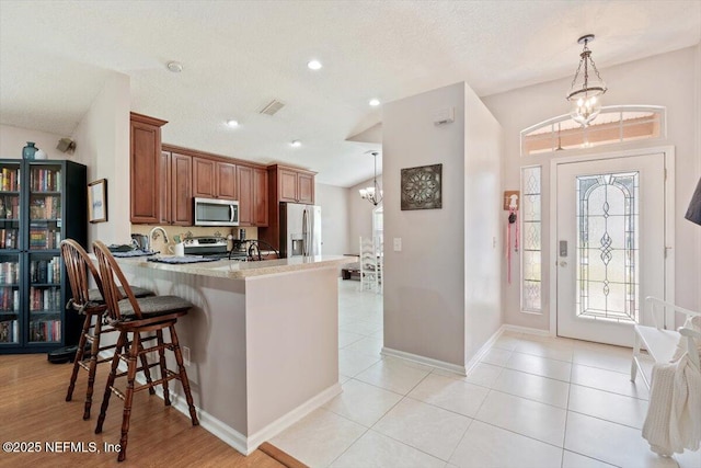 kitchen with decorative light fixtures, an inviting chandelier, kitchen peninsula, a breakfast bar, and stainless steel appliances