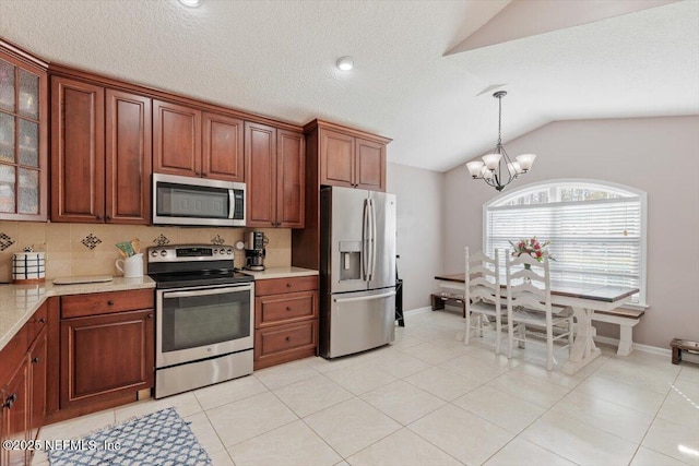 kitchen featuring pendant lighting, appliances with stainless steel finishes, lofted ceiling, an inviting chandelier, and light tile patterned floors