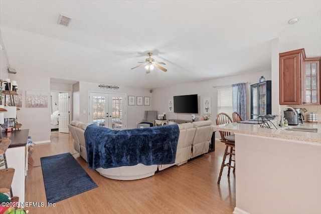 living room with ceiling fan, sink, french doors, and light wood-type flooring