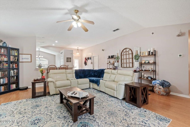 living room with vaulted ceiling, ceiling fan with notable chandelier, light hardwood / wood-style floors, and a textured ceiling