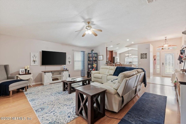 living room with ceiling fan with notable chandelier, light hardwood / wood-style flooring, a textured ceiling, and lofted ceiling