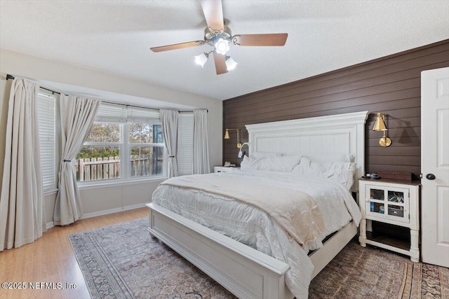 bedroom featuring ceiling fan, a textured ceiling, wood walls, and light wood-type flooring