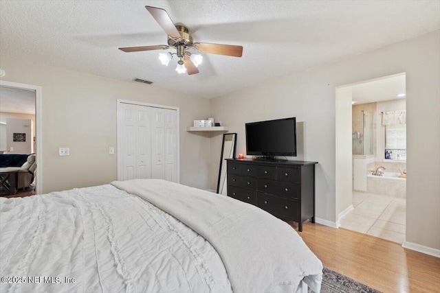 bedroom with a textured ceiling, ensuite bath, a closet, ceiling fan, and light hardwood / wood-style flooring