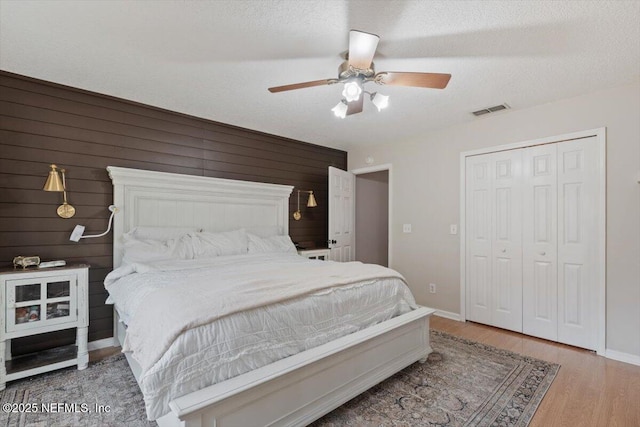 bedroom with a textured ceiling, wood-type flooring, a closet, wood walls, and ceiling fan