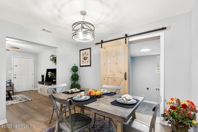 dining space featuring wood-type flooring, a notable chandelier, and a barn door