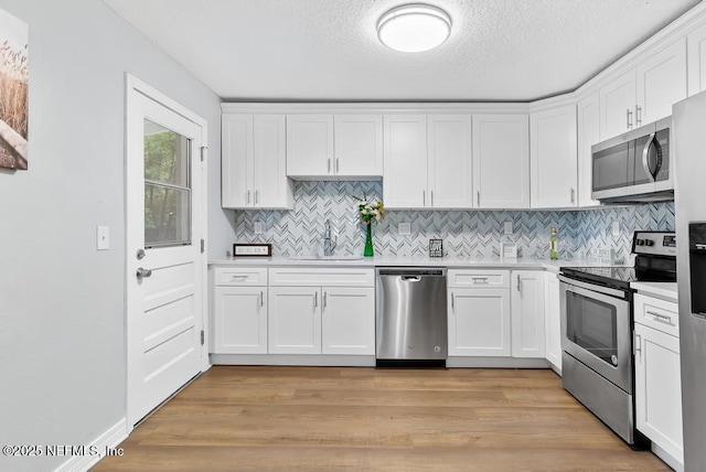 kitchen featuring appliances with stainless steel finishes, a textured ceiling, white cabinets, sink, and light hardwood / wood-style flooring