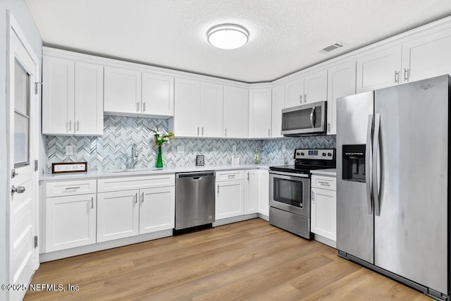 kitchen with sink, light wood-type flooring, white cabinetry, a textured ceiling, and stainless steel appliances