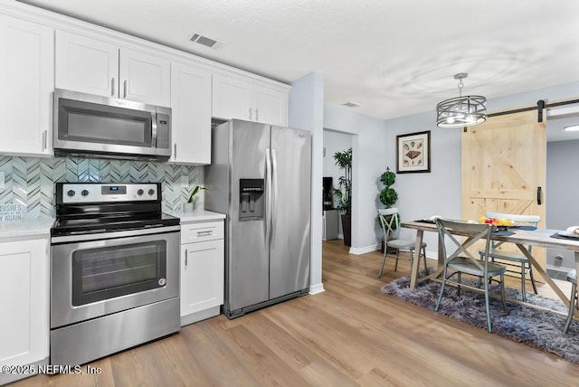 kitchen with backsplash, white cabinetry, a barn door, and appliances with stainless steel finishes