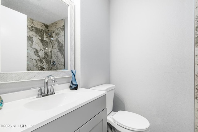 bathroom featuring toilet, vanity, and a tile shower