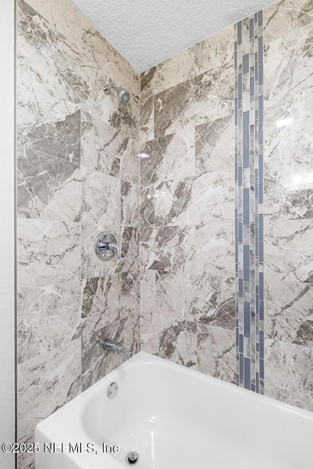 bathroom with a textured ceiling and tiled shower / bath