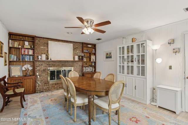 dining space with ceiling fan, a fireplace, and built in shelves