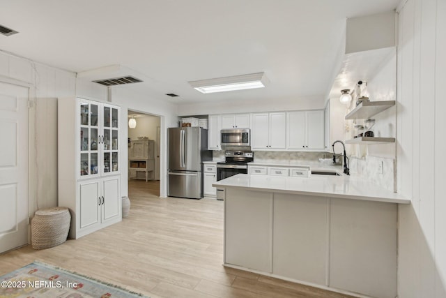 kitchen featuring appliances with stainless steel finishes, white cabinetry, sink, decorative backsplash, and kitchen peninsula