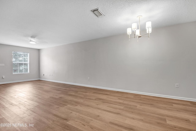 spare room with an inviting chandelier, light hardwood / wood-style floors, and a textured ceiling