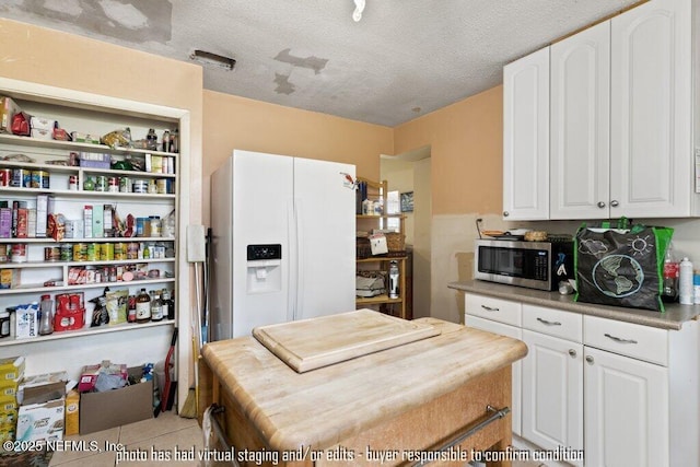 kitchen with white cabinetry, light tile patterned floors, white fridge with ice dispenser, and a textured ceiling