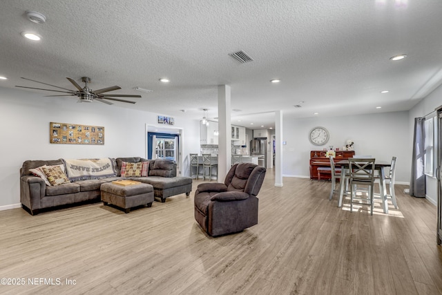 living room featuring ceiling fan, a textured ceiling, and light wood-type flooring