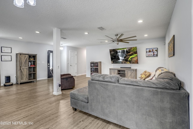 living room with ceiling fan, a barn door, hardwood / wood-style floors, and a textured ceiling