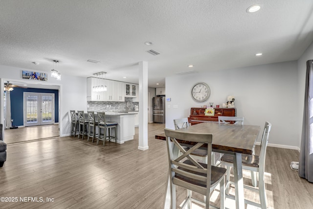 dining area with french doors, a textured ceiling, and light wood-type flooring