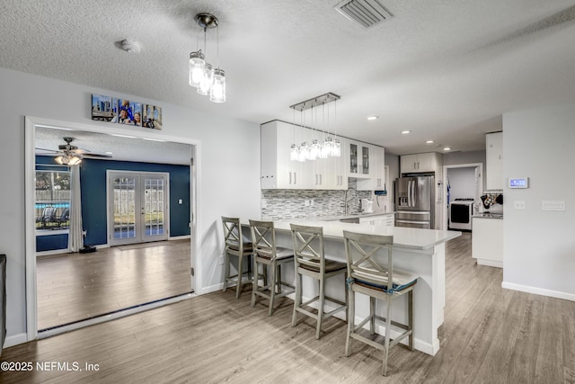 kitchen featuring french doors, hanging light fixtures, stainless steel fridge, kitchen peninsula, and white cabinets