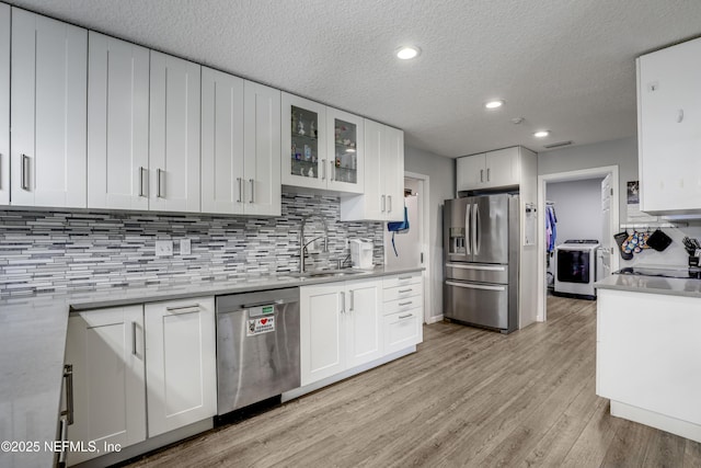 kitchen featuring washer / dryer, sink, white cabinetry, light wood-type flooring, and appliances with stainless steel finishes