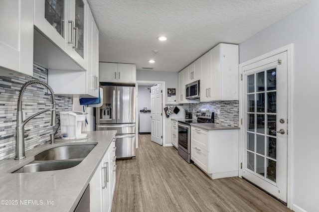 kitchen with sink, light wood-type flooring, white cabinets, stainless steel appliances, and a textured ceiling