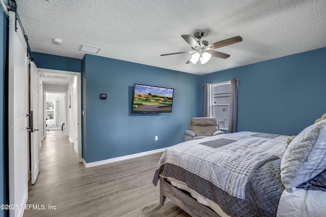 bedroom with ceiling fan, a barn door, a textured ceiling, and light wood-type flooring