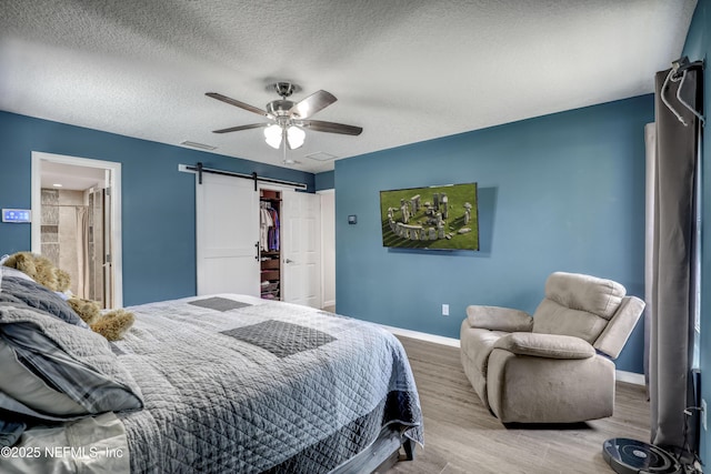 bedroom with hardwood / wood-style flooring, ceiling fan, a textured ceiling, a barn door, and a closet