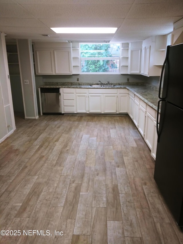 kitchen with white cabinets, black refrigerator, light hardwood / wood-style floors, sink, and light stone counters