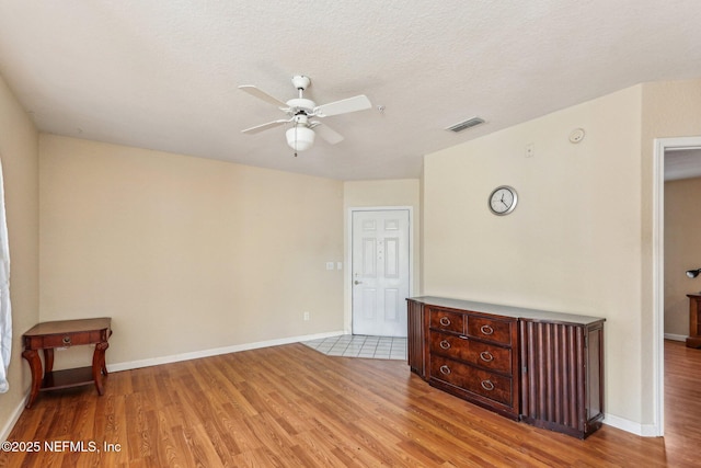 unfurnished room with a textured ceiling, ceiling fan, and light wood-type flooring