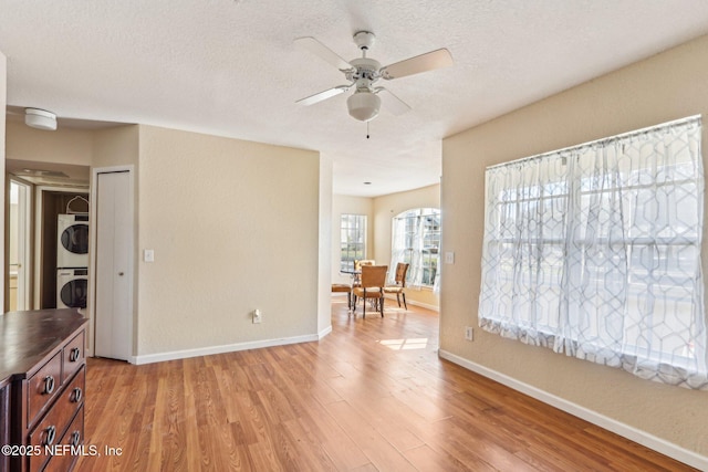 unfurnished room with stacked washer / dryer, ceiling fan, a textured ceiling, and light hardwood / wood-style flooring