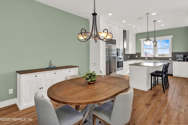 dining space with sink, light hardwood / wood-style floors, and a notable chandelier