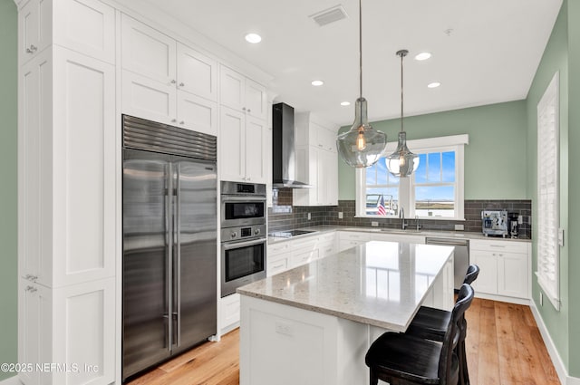 kitchen with wall chimney exhaust hood, appliances with stainless steel finishes, a center island, and white cabinets