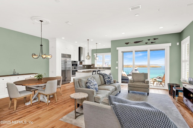 living room with an inviting chandelier, light hardwood / wood-style floors, and a water view