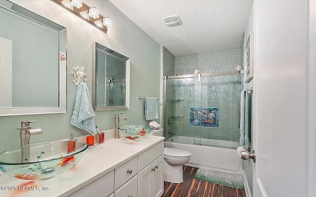 full bathroom featuring toilet, shower / bath combination with glass door, a textured ceiling, vanity, and hardwood / wood-style flooring