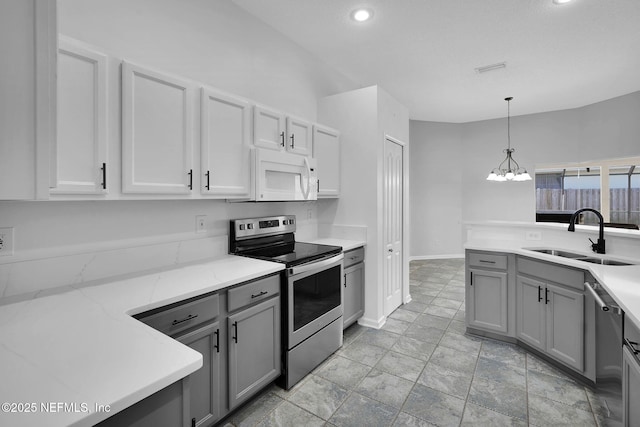 kitchen with hanging light fixtures, sink, gray cabinetry, light stone counters, and stainless steel appliances