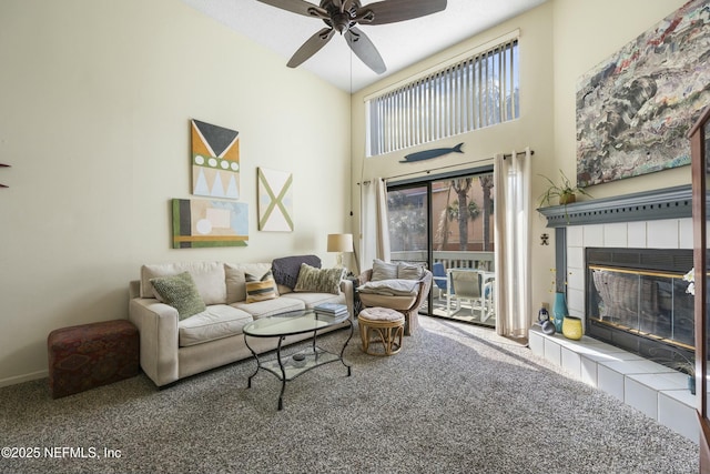 carpeted living room with ceiling fan, a tiled fireplace, and a high ceiling