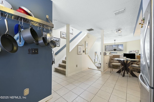 interior space featuring hanging light fixtures, stainless steel fridge, a textured ceiling, and light tile patterned flooring