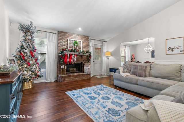 living room with vaulted ceiling, a brick fireplace, a healthy amount of sunlight, and dark hardwood / wood-style floors