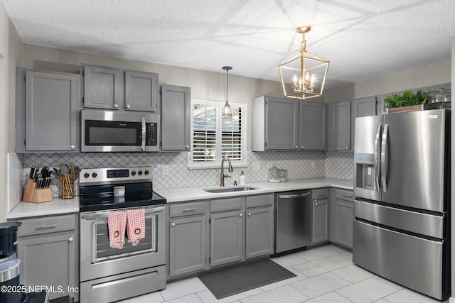 kitchen featuring pendant lighting, sink, gray cabinetry, decorative backsplash, and stainless steel appliances