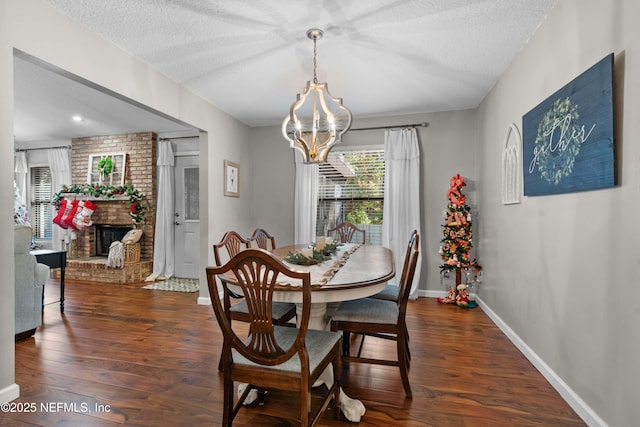 dining space featuring a brick fireplace, a textured ceiling, dark hardwood / wood-style flooring, and an inviting chandelier