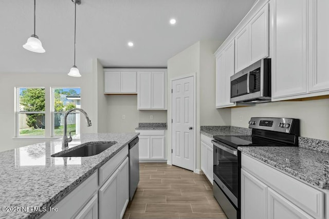 kitchen featuring appliances with stainless steel finishes, sink, decorative light fixtures, white cabinets, and light stone counters