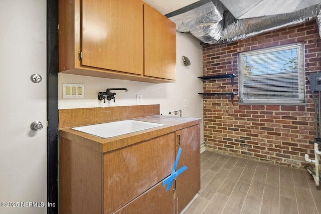 kitchen with brick wall, sink, and light wood-type flooring