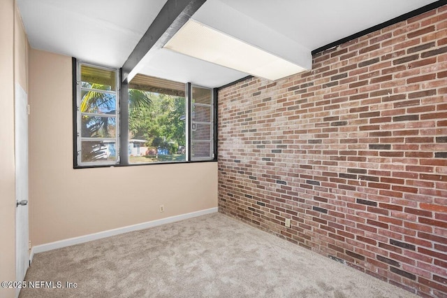 carpeted spare room with brick wall and beam ceiling