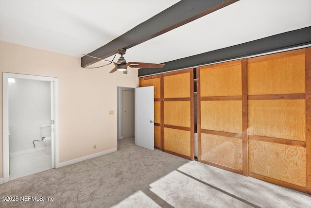 unfurnished bedroom featuring beamed ceiling, light colored carpet, ensuite bathroom, and ceiling fan