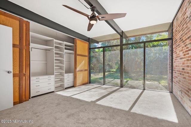 interior space with ceiling fan, brick wall, light carpet, and multiple windows