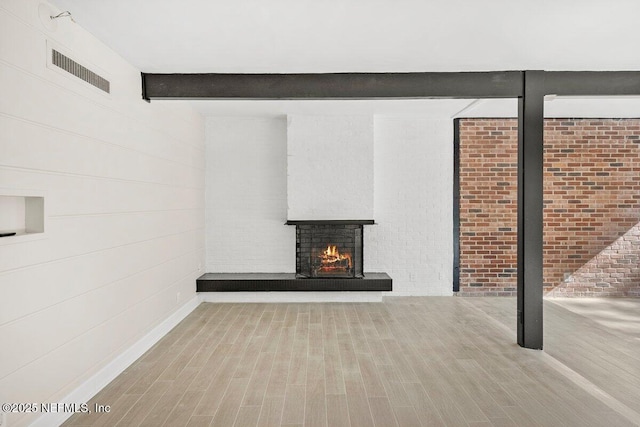 interior space with a brick fireplace, beam ceiling, light wood-type flooring, and brick wall