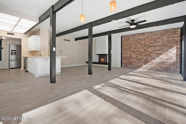 unfurnished living room featuring a multi sided fireplace, brick wall, sink, ceiling fan, and light hardwood / wood-style flooring