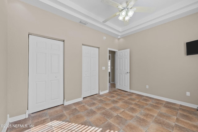 unfurnished bedroom featuring two closets, ceiling fan, and a tray ceiling