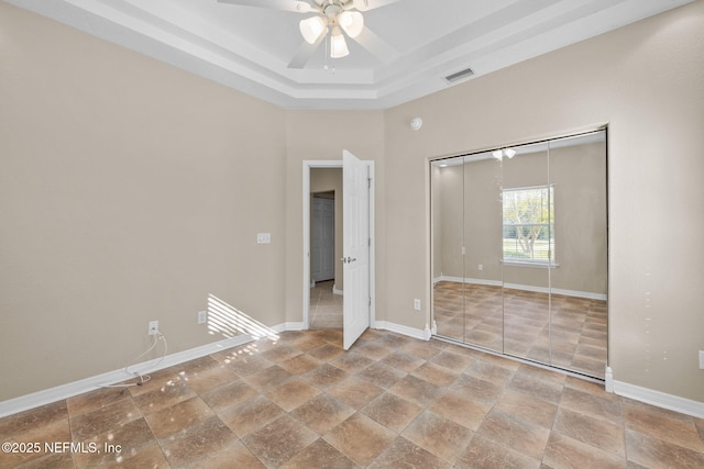 unfurnished bedroom with a tray ceiling, a closet, and ceiling fan