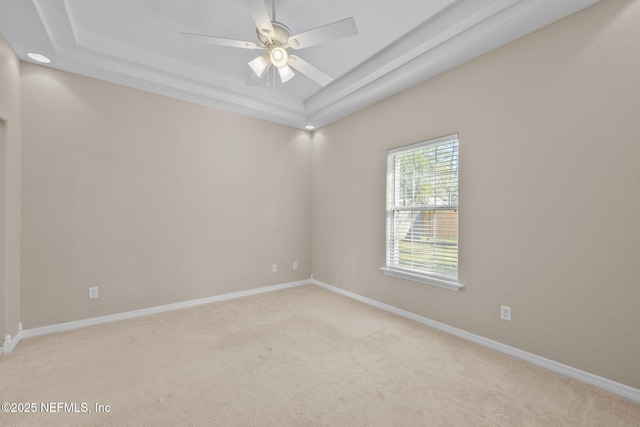 empty room featuring ceiling fan, a raised ceiling, and light carpet